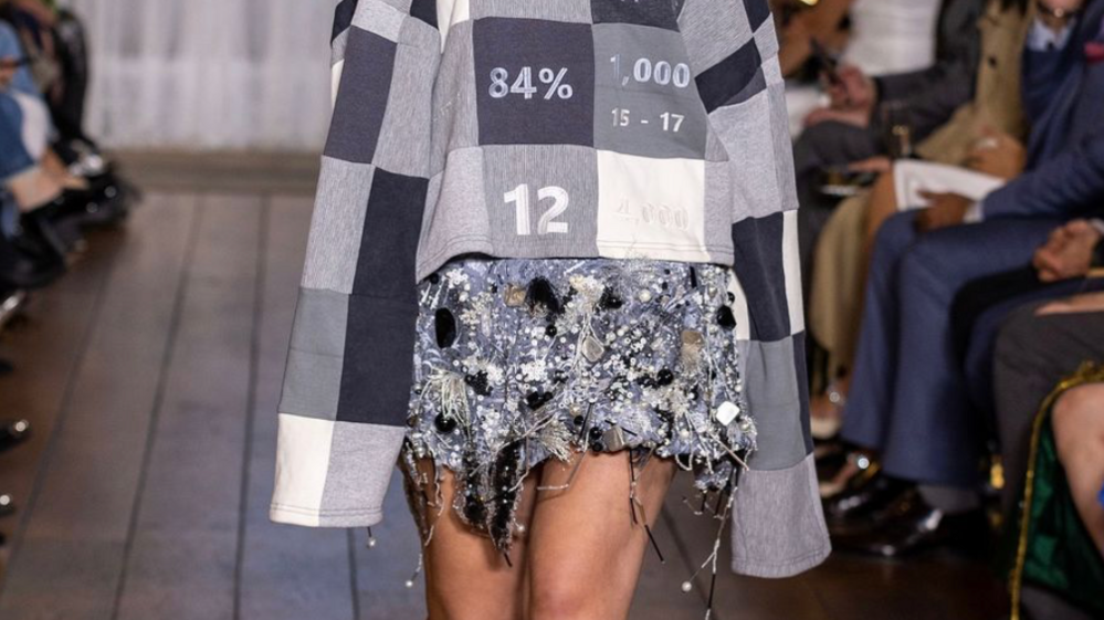 A model walking the runway wearing grey sweatshirt and silver embellished skirt.