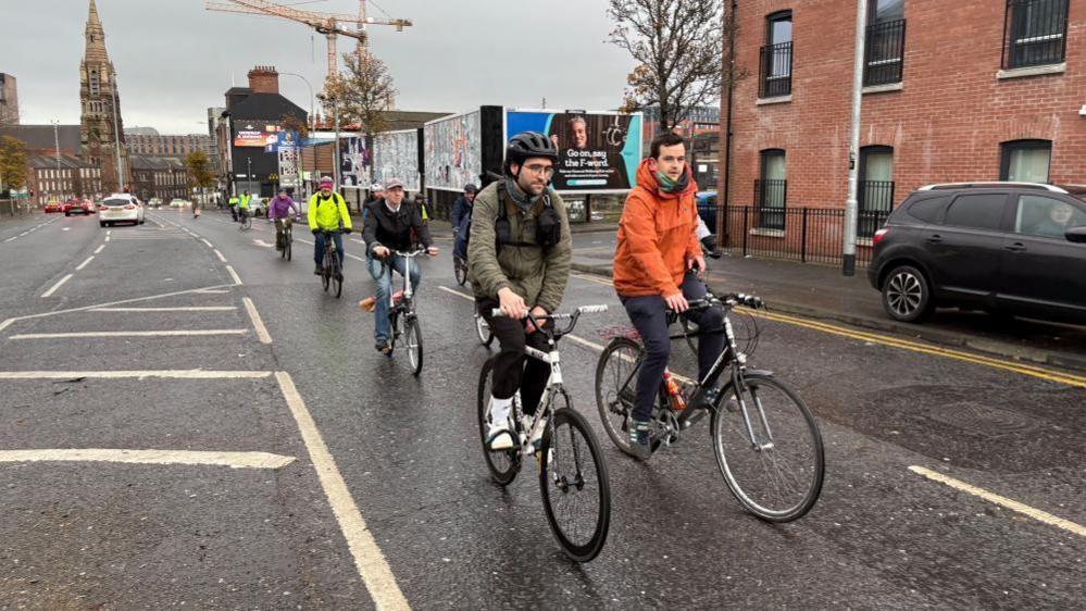 A group of cyclists wearing high vis colours and helmets are cycling along the road. 