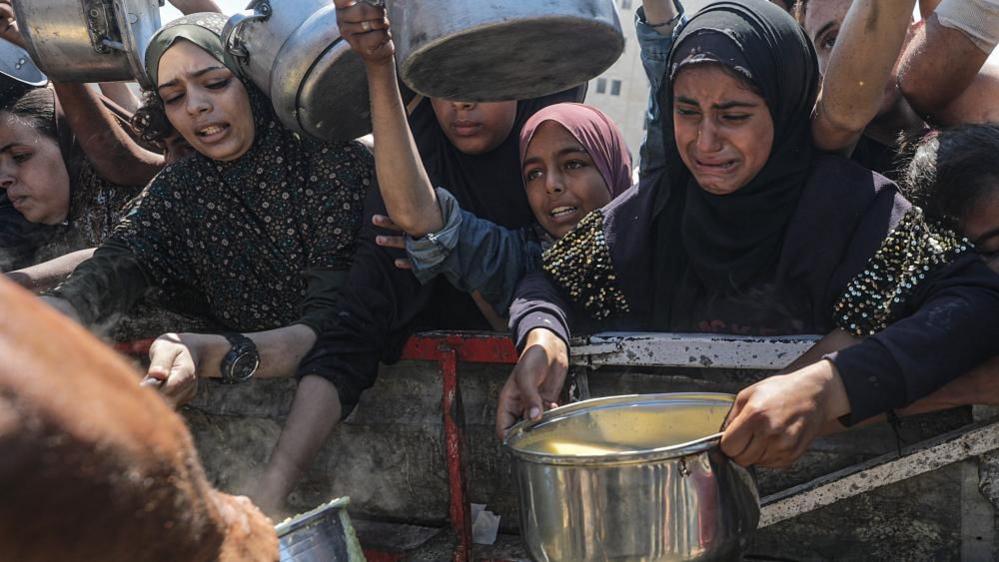Internally displaced Palestinians, including children, hold pots as they receive food from a charity kitchen