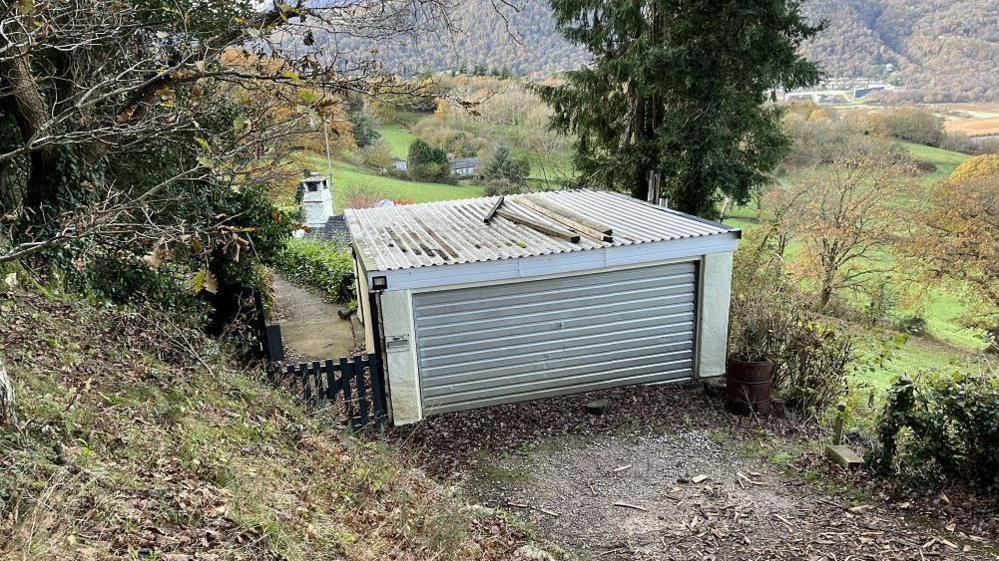 Separate garage with door closed and gate to the left to footpath which leads down a hill.