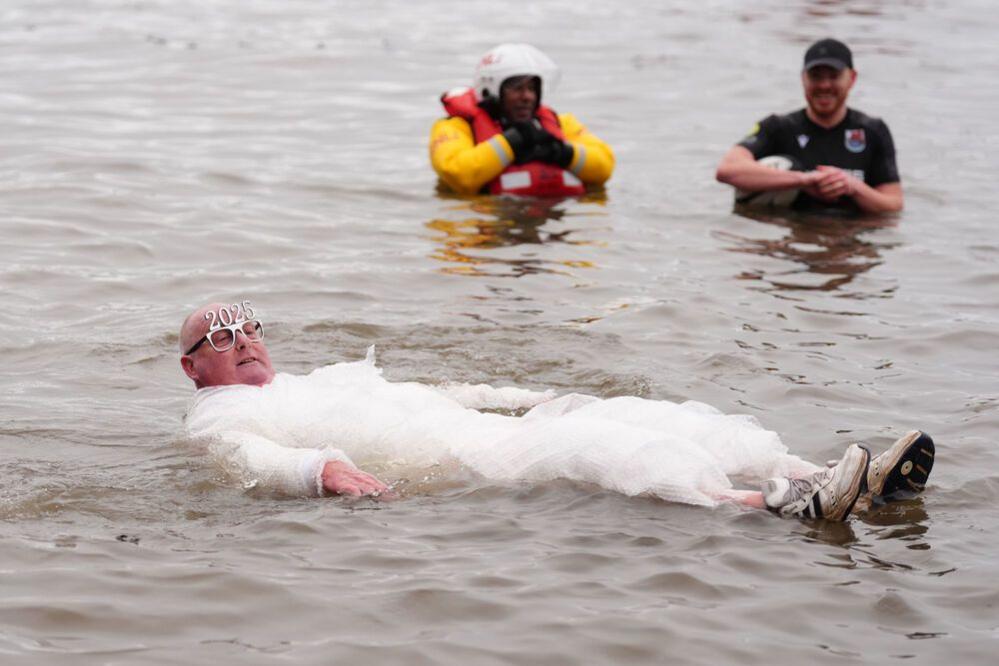 A man wrapped in bubble wrap floats in the water with 2025 glasses.