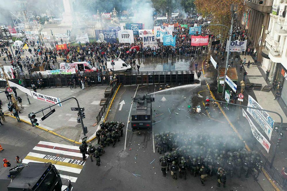 An aerial view shows police and demonstrators in the streets of Buenos Aires with a water cannon and tear gas firing, on 12 June