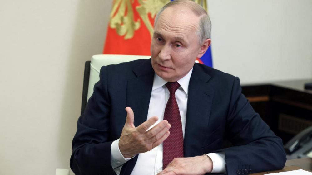 Putin gestures as he speaks, sitting at a desk in the Kremlin