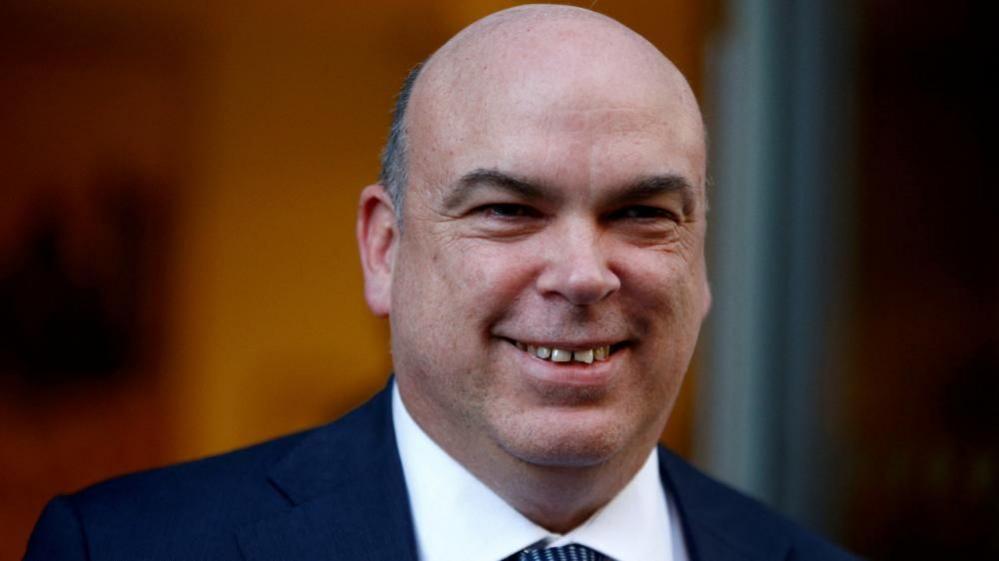 Mike Lynch smiling in blue suit, white shirt and blue tie