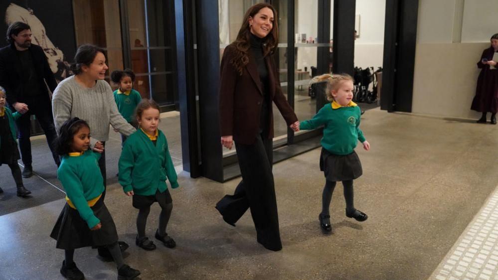 Catherine, Princess of Wales enters the National Portrait  Gallery holding the hand of a young girl from the school