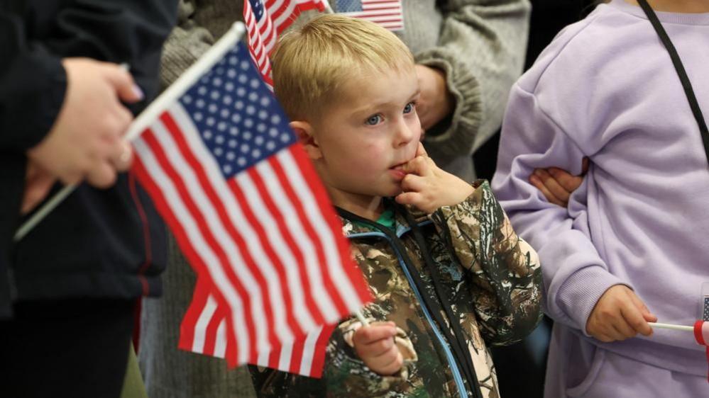 People from the first group of white South Africans granted refugee status in the US hold US flags as they attend a meet and greet event, at Dulles International Airport