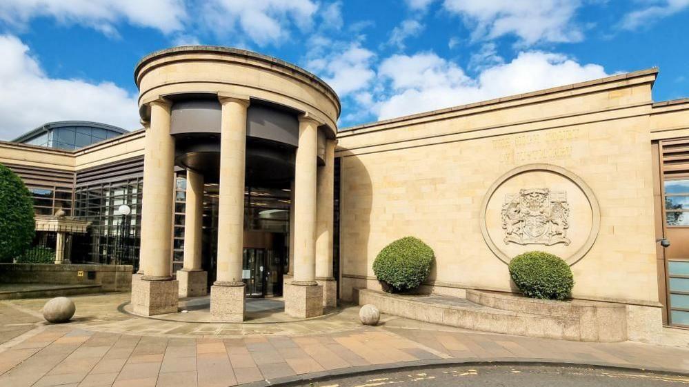 An exterior view of the entrance to the High Court in Glasgow captured under a blue sky with some clouds in the air.