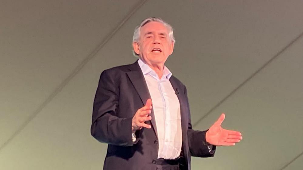 Gordon Brown standing on a stage with his palms pointing outwards