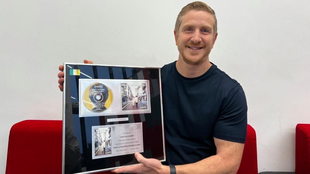 Anthony Lanni, holding his platinum disc that shows artwork for (What's the Story) Morning Glory? 