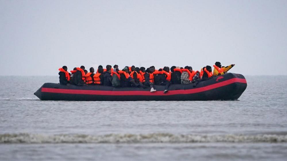 A group of of around 30 people wearing orange life jackets crammed onto a small boat in the English Channel