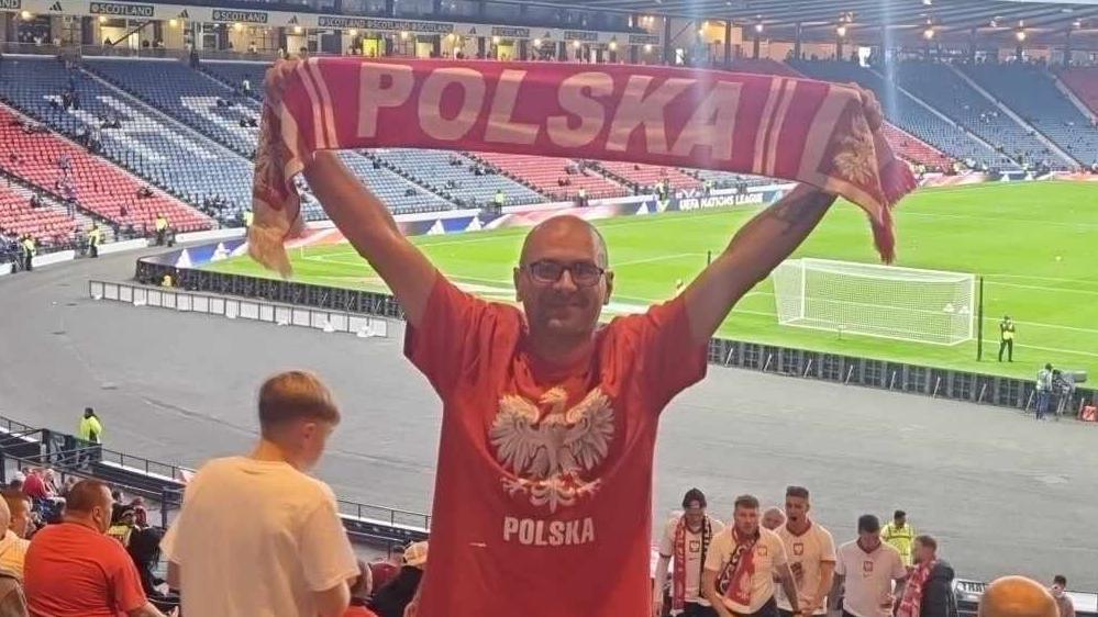 Jaroslaw Rossa at a football match holds a Polska scarf over his head.