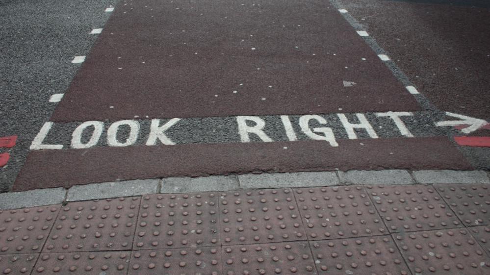 The floor of a pedestrian crossing, with knobbly textured tiles on the edge of the footpath. There is also writing on the floor that says "look right".