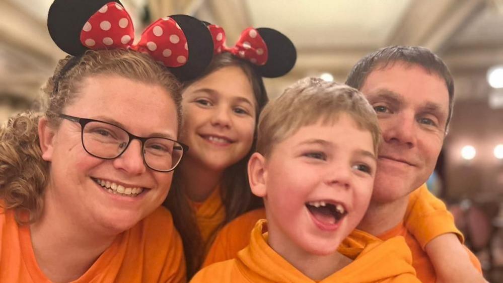 The Tilley family wearing orange T-shirts. Aimee and Eva are wearing Mini Mouse headbands. 