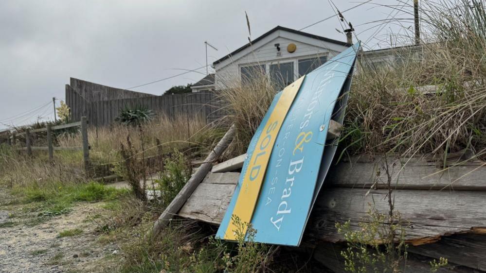 A "for sale" sign, on it;s side having fallen over, belonging to Minors and Brady, which is blue and yellow. Behind it is a house which was reported to have been sold, but no details of the sale proceeding have been confirmed.
