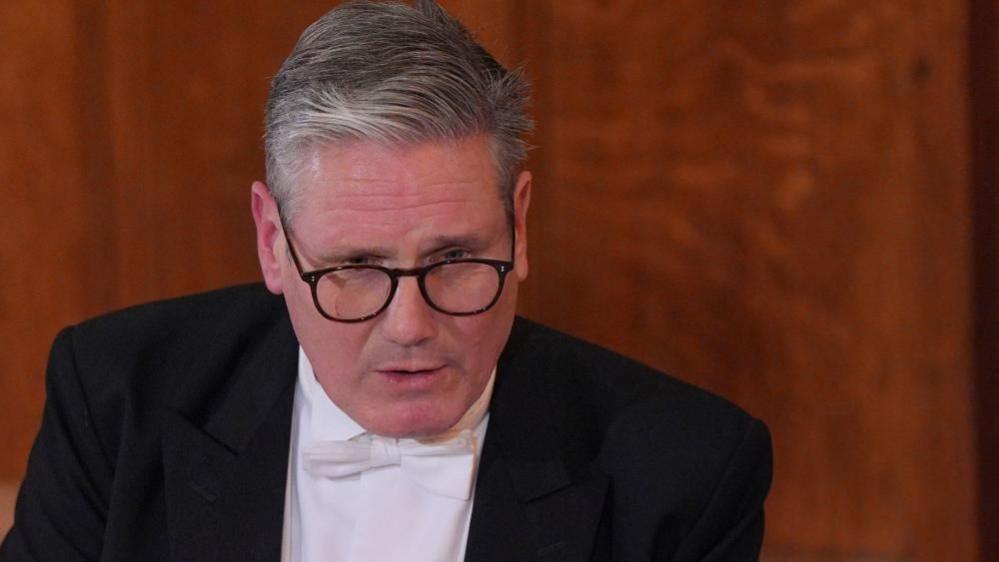 Keir Starmer in a white shirt, bow tie and black jacket giving a speech