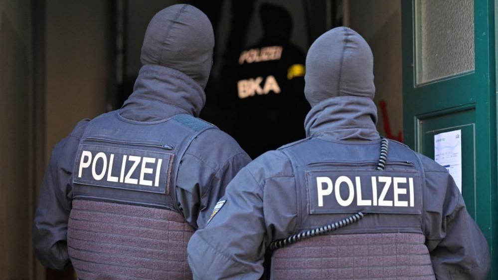 Two German police officers wearing hoods pictured outside a house from behind.