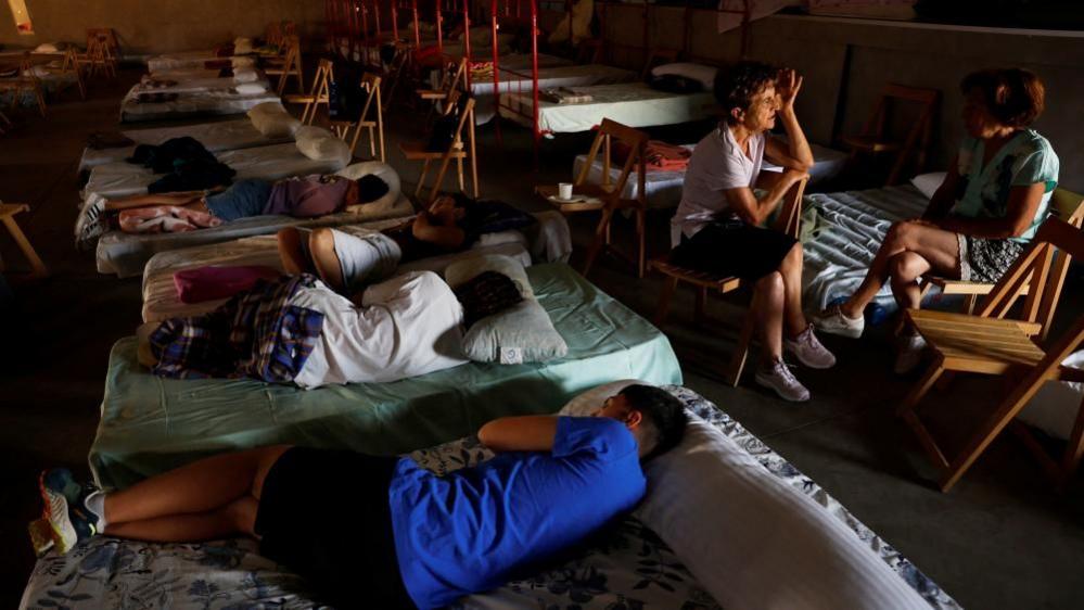 People lying on mattresses on the floor in a shelter