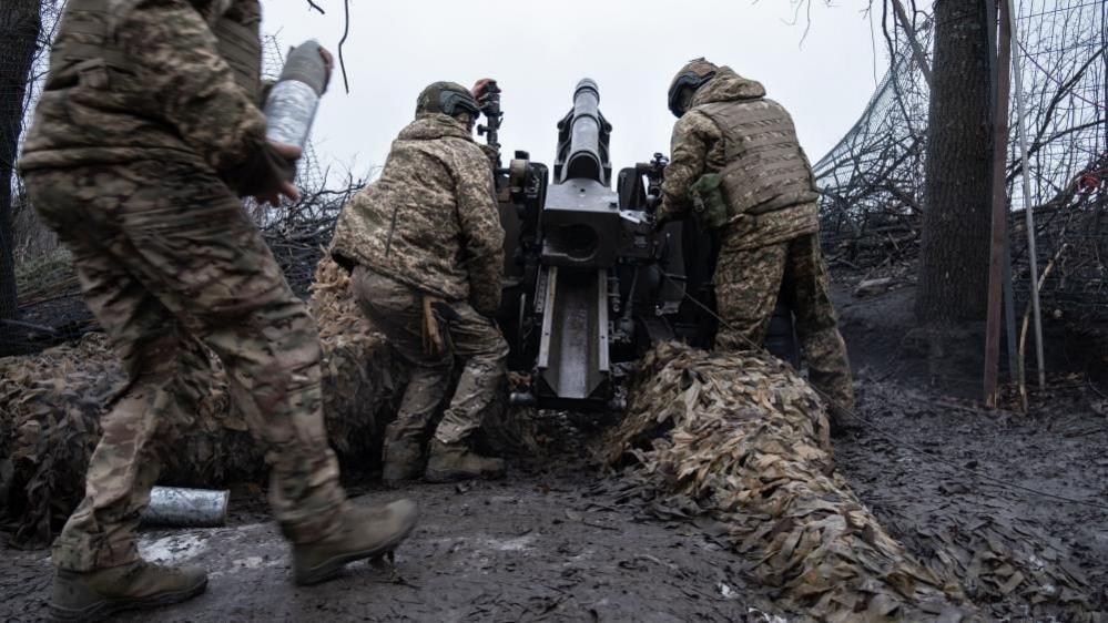 Ukrainian soldiers preparing to fire a howitzer in the Kharkiv region - three men wearing camouflage load the gun, 18 Jan 25.