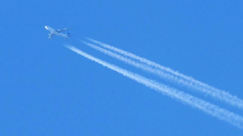 photo of an airplane flying in blue skies with a condenstation trail behind.
