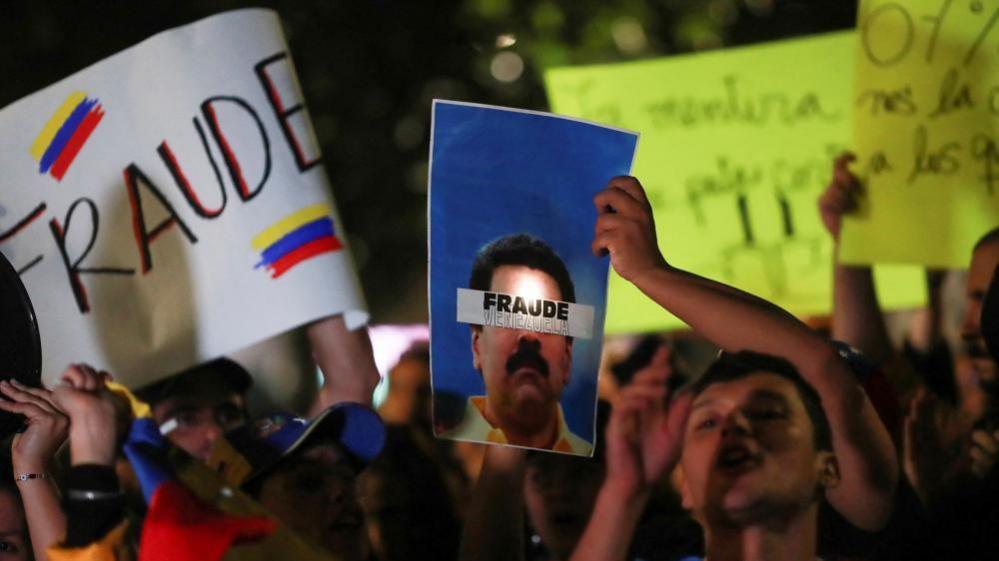 A man holds a poster beside other Venezuelans living in Mexico and members of Comando ConVzla during a protest against the election results that awarded Venezuelan President Nicolas Maduro a third term, in front of the Angel of Independence monument in Mexico City, Mexico July 30, 2024.