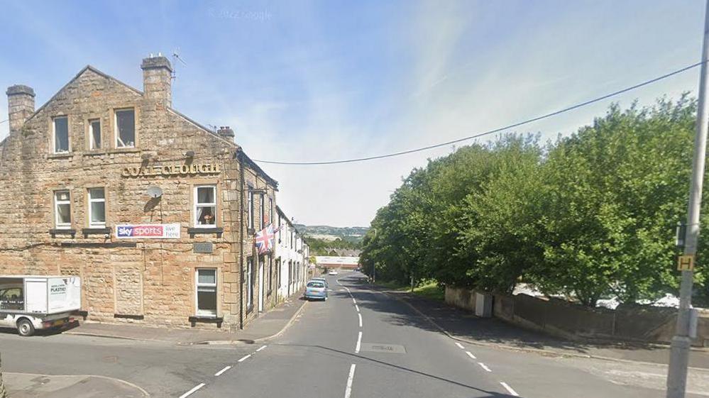 Coal Clough pub, Burnley, on the left of Coal Clough Lane, with trees lining the road on the right