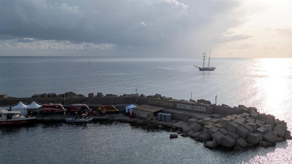 A drone view shows emergency and rescue service vehicles and personnel at a port near the site where a luxury yacht sank, in Porticello