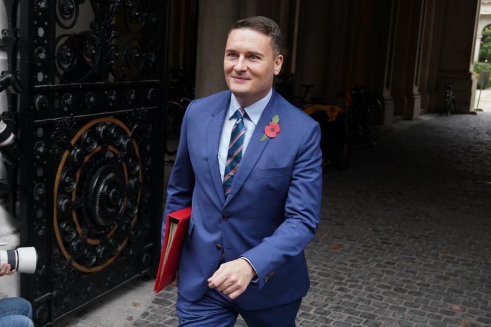 Wes Streeting in a suit, smiling, wearing a poppy