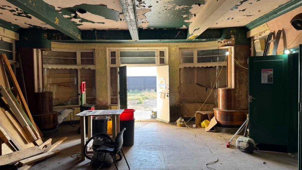The interior of the Iron Duke, showing some builders' materials and doors stacked against the walls. Paint has peeled from the ceilings.