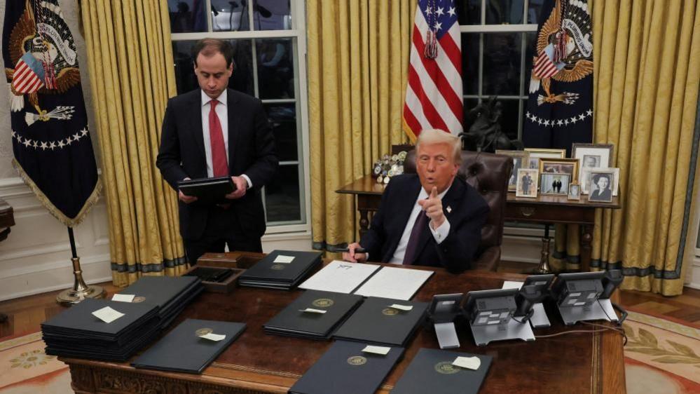 US President Donald Trump signs documents as he issues executive orders and pardons for January 6 defendants in the Oval Office 