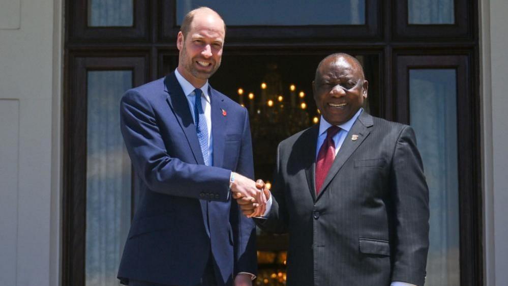 Prince William and Ramaphosa shake hands outside a doorway