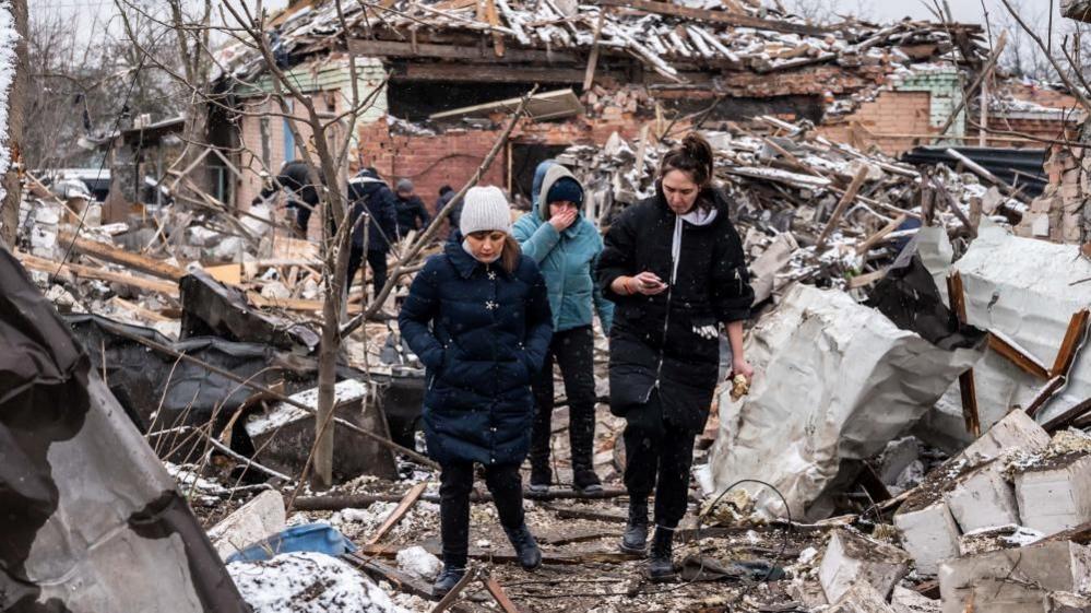 Women walk among remains of residential buildings destroyed by shelling, as Russias invasion of Ukraine continues, in Zhytomyr