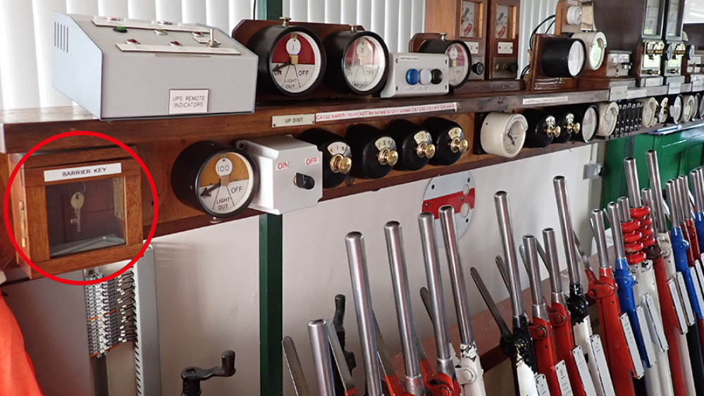 A row of railway signalling levers, with a key inside a wood and glass box circled on the left side of the picture