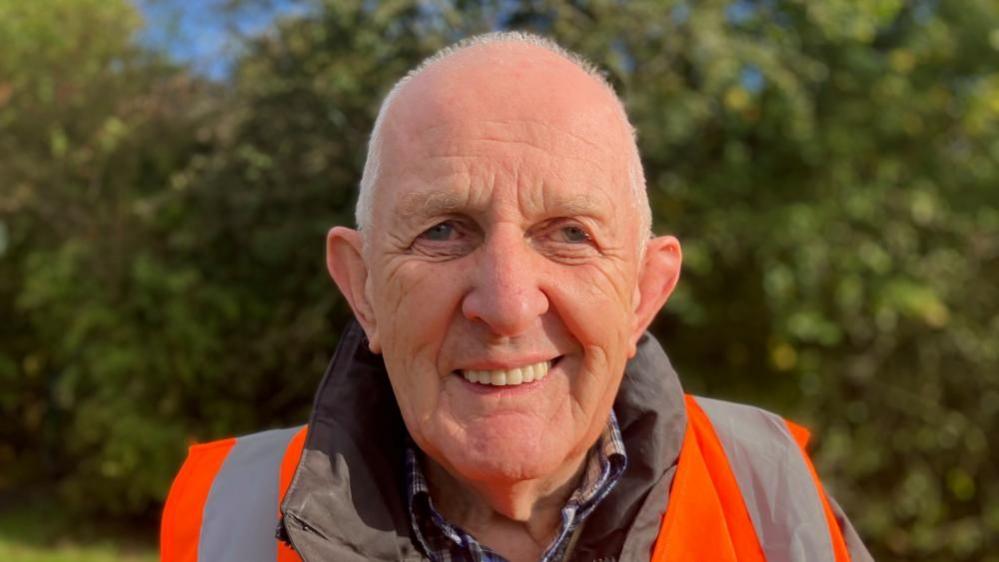 An older man wearing a orange high vis jacket