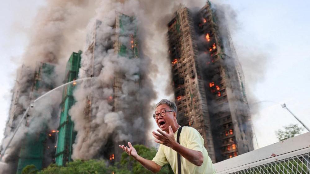 A man gestures in distress as the tower blocks burn behind him.