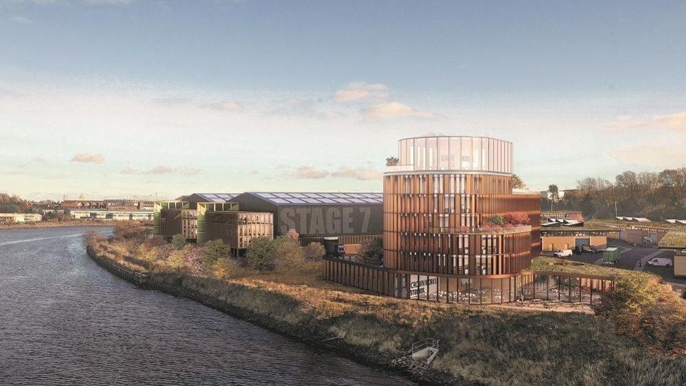 A CGI of how Crown Works Studios could look once built. A large glass building stands overlooking the river. Next to it are large warehouse-like structures. The nearest one has Studio 7 painted across one of its outer walls.