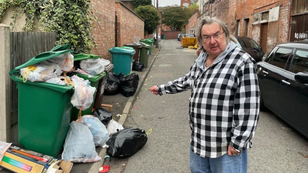 Michael Eaton, who lives on Lawson Street, stood in the road pointing at overflowing rubbish on the road.