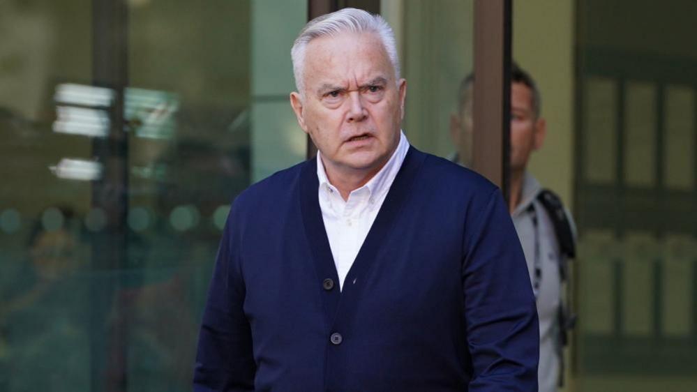 Huw Edwards in a blue cardigan walking out of court after his sentencing