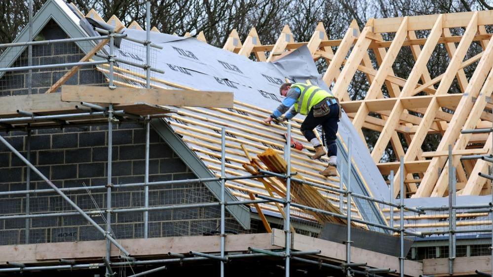 Workman in hi-vis working on the roof of an unfinished house