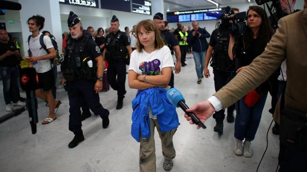 Swedish activist Greta Thunberg walks inside a terminal surrounded by journalists and French police at the Paris-Charles de Gaulle Airport.