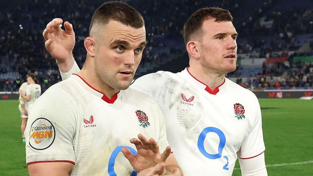 Ben Earl (left) claps his hands as Ben Spencer (right) holds his arm in the air behind him as the two stand together on the pitch following full-time of England v France