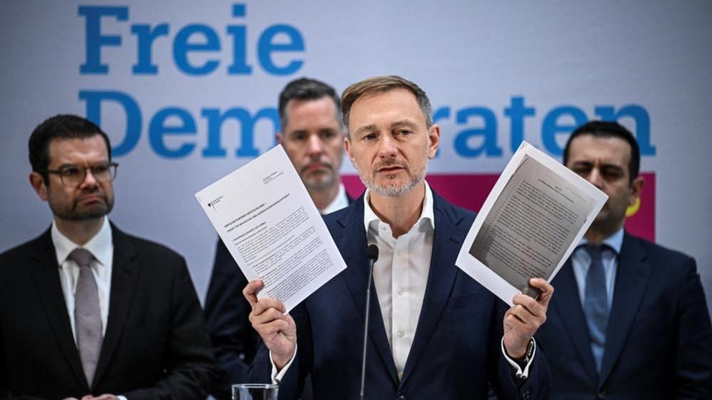 Christian Lindner holds up documents as he speaks to reporters after he was sacked by Olaf Scholz