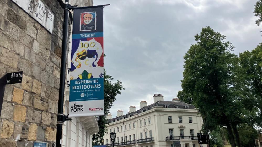 Wilbur's theatre-themed painting is printed on a banner, underneath an image of Joseph Rowntree and the word Theatre. Underneath, it says "inspiring the next 100 years".