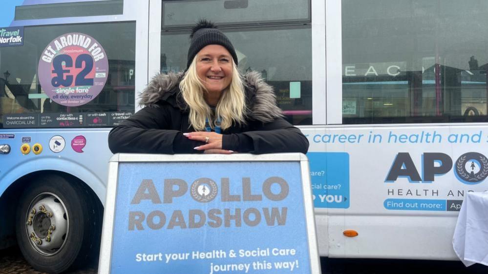 Debbie Sampson standing and leaning on an advertising board for the Apollo Roadshow