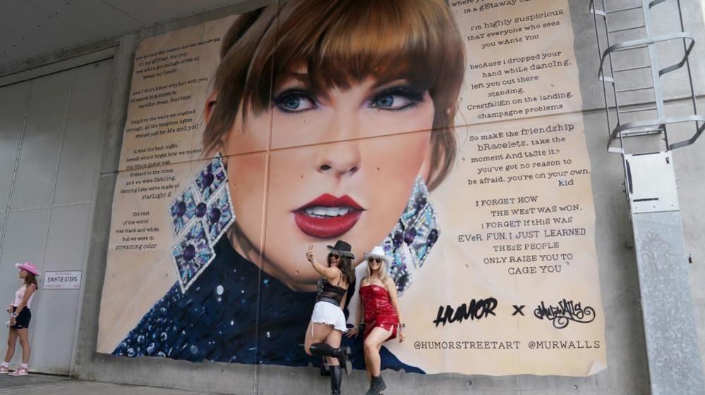 Two women in front of Taylor Swift mural