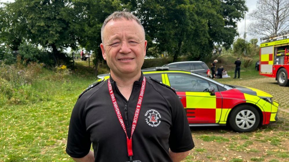 Darren Carson with short light-coloured hair wearing a fire service shirt in front of a fire service vehicle