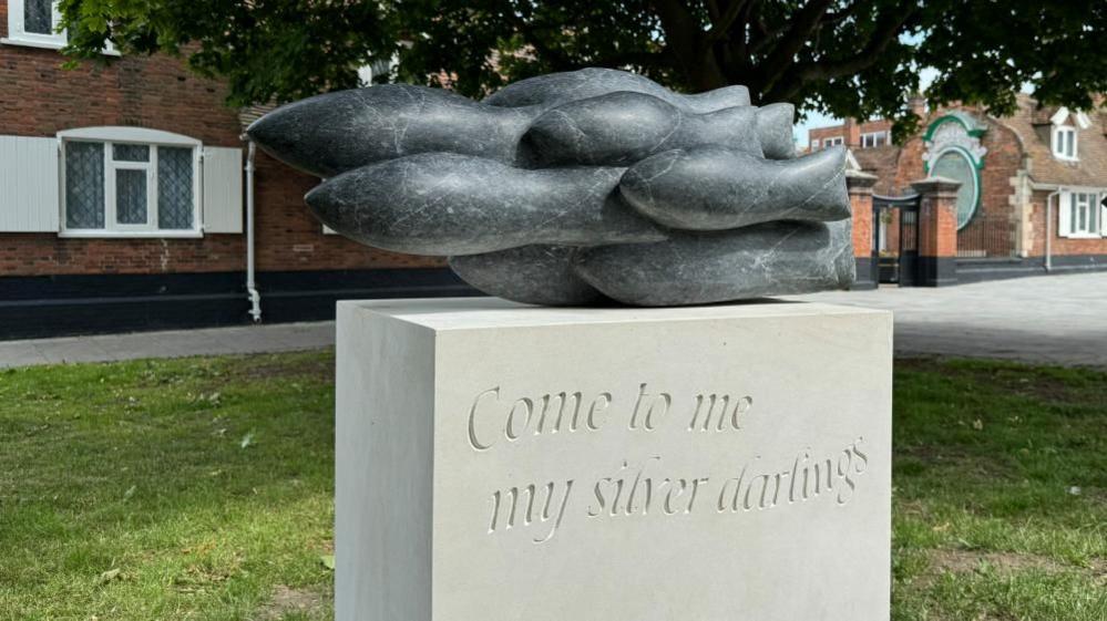 A stone plinth with a granite abstract of a shoal of herring, mounted outside Great Yarmouth's Fishermen's Hospital.