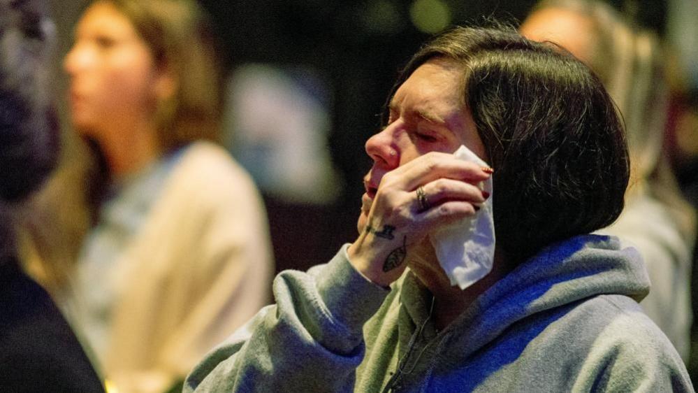 A woman holds a tissue to her face while praying for the victims and survivors of a US school shooting