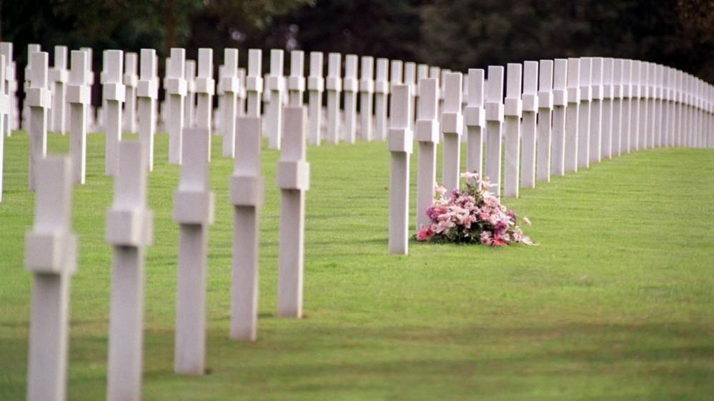 A pink floral wreath sitting among white crosses