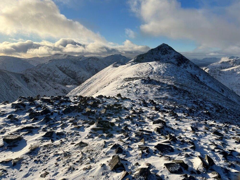 A mountain ridge covered in snow with clouds and a blue sky