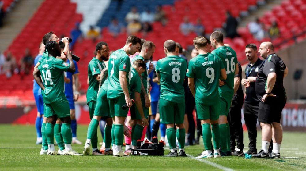 Wakering players in green strip gather on the pitch